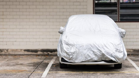 A white sedan sits in a parking lot under a vehicle cover, shielded from the elements.