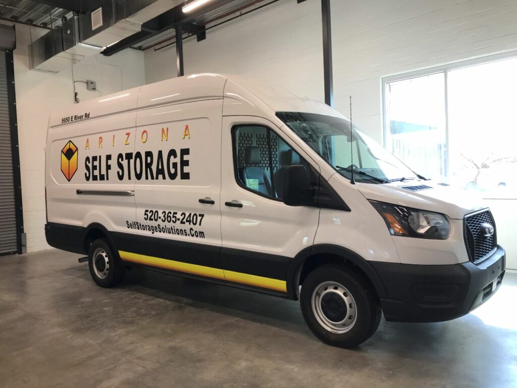 A white moving truck with the Arizona Self Storage logo on the side is parked inside of a loading bay