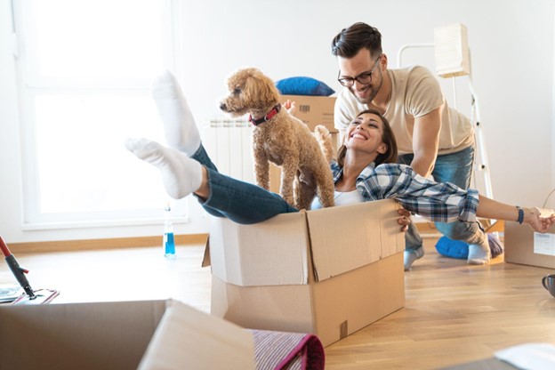 A couple playfully push around boxes with their dog during a move